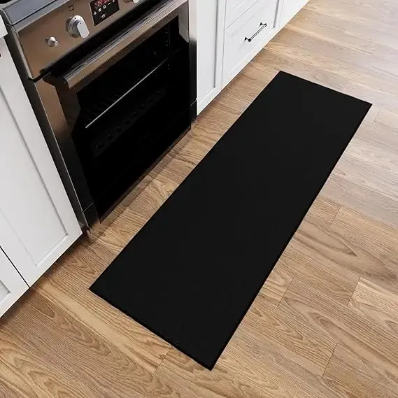 Black anti-fatigue kitchen runner mat in front of stainless steel oven and white cabinets